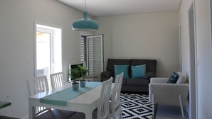 A modern living room with a dining area, featuring a sofa, chairs, a table, and a hanging light fixture.