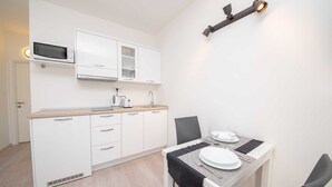 A modern kitchen with white cabinetry, a microwave, a kettle, and a toaster. There is a dining table with a black table runner and white plates. - Cosy studio Stone for 2 with large balcony (Bol)