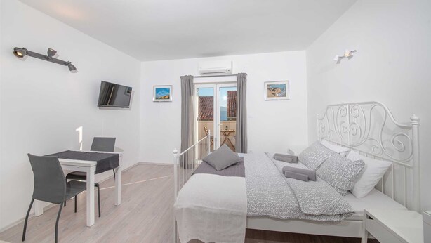 A bedroom with a bed, a desk, and a chair. There is a TV on the wall and a window with curtains. - Cosy studio Stone for 2 with large balcony (Bol)