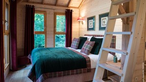 A cozy wooden cabin bedroom with a bed, red curtains, a ladder, and framed pictures on the wall. - LUXURY CABIN WITH SPA IN TREES (La Bussiere)