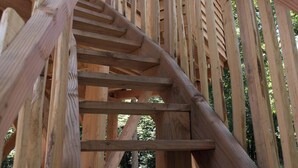 A wooden spiral staircase leading to a wooden structure with a sloped roof, surrounded by trees. - LUXURY CABIN WITH SPA IN TREES (La Bussiere)
