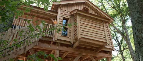 A wooden treehouse with a balcony, built on stilts, surrounded by trees.