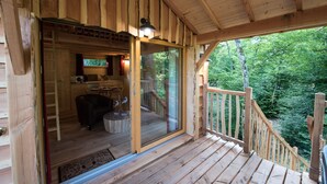 A wooden cabin with a glass door leading to a dining area and a balcony overlooking a forest. - LUXURY CABIN WITH SPA IN TREES (La Bussiere)