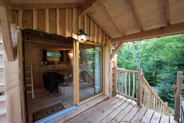 A wooden cabin with a glass door leading to a dining area and a balcony overlooking a forest.