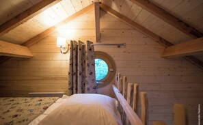 Een gezellig slaapkamer onder de pannen met houten wanden, een rond raam, een bed met een wit kussen en gordijnen met uilenprint.