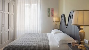 Ein ordentlich bezogenes Bett mit einem gemusterten Überwurf, einer Nachttischlampe und einem Nachttisch mit einem Glas und einem Gefäß.
