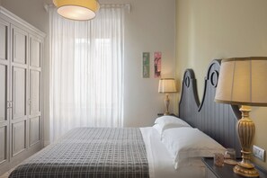 Un lit bien fait, recouvert d’une couvre-lit à motifs, une lampe de chevet et une table de chevet avec un pot et un verre.
