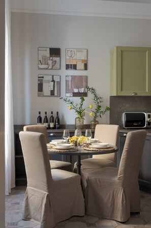 A dining area with a round table, four chairs, a vase with flowers, and wine bottles on a shelf.