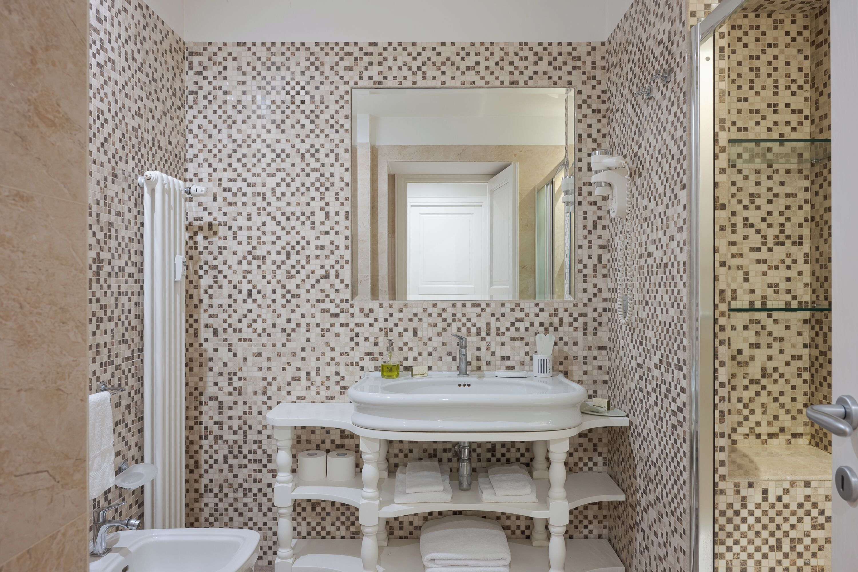 A bathroom with a tiled wall, a sink, a mirror, a shower, and a toilet.