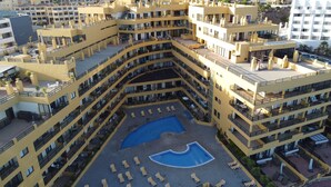 Ein mehrstöckiges Hotel mit Innenhof, der einen Pool und Liegestühle beinhaltet.