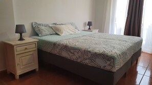 Una cama bien hecha con ropa de cama estampada, dos mesitas de noche con lámparas y una ventana con cortinas.