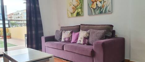 Ein Wohnzimmer mit einem violetten Sofa, einem Glastisch und zwei Bildern an der Wand.