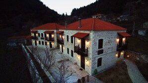 Um edifício de pedra com várias varandas e telhado de telhas vermelhas, rodeado por uma paisagem montanhosa.