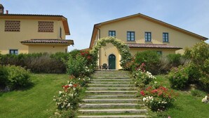 A two-story building with a green door, surrounded by a garden with a stone staircase leading to the entrance. - SANGIOVESE APARTMENT at Agriturismo MUSIGNANO (Cerreto guidi)