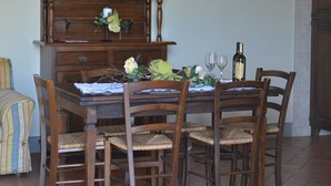 A dining area with a wooden table set for four, surrounded by wicker chairs. A cabinet with glass doors is above the table, and a wall-mounted light fixture is visible. - SANGIOVESE APARTMENT at Agriturismo MUSIGNANO (Cerreto guidi)