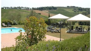 A pool area with lounge chairs and umbrellas, surrounded by lush greenery and hills in the background. - SANGIOVESE APARTMENT at Agriturismo MUSIGNANO (Cerreto guidi)