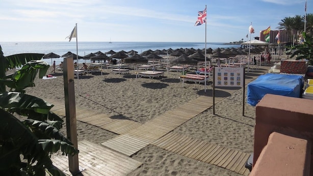 Ein Strand mit Sonnenschirmen, Liegestühlen und Flaggen.