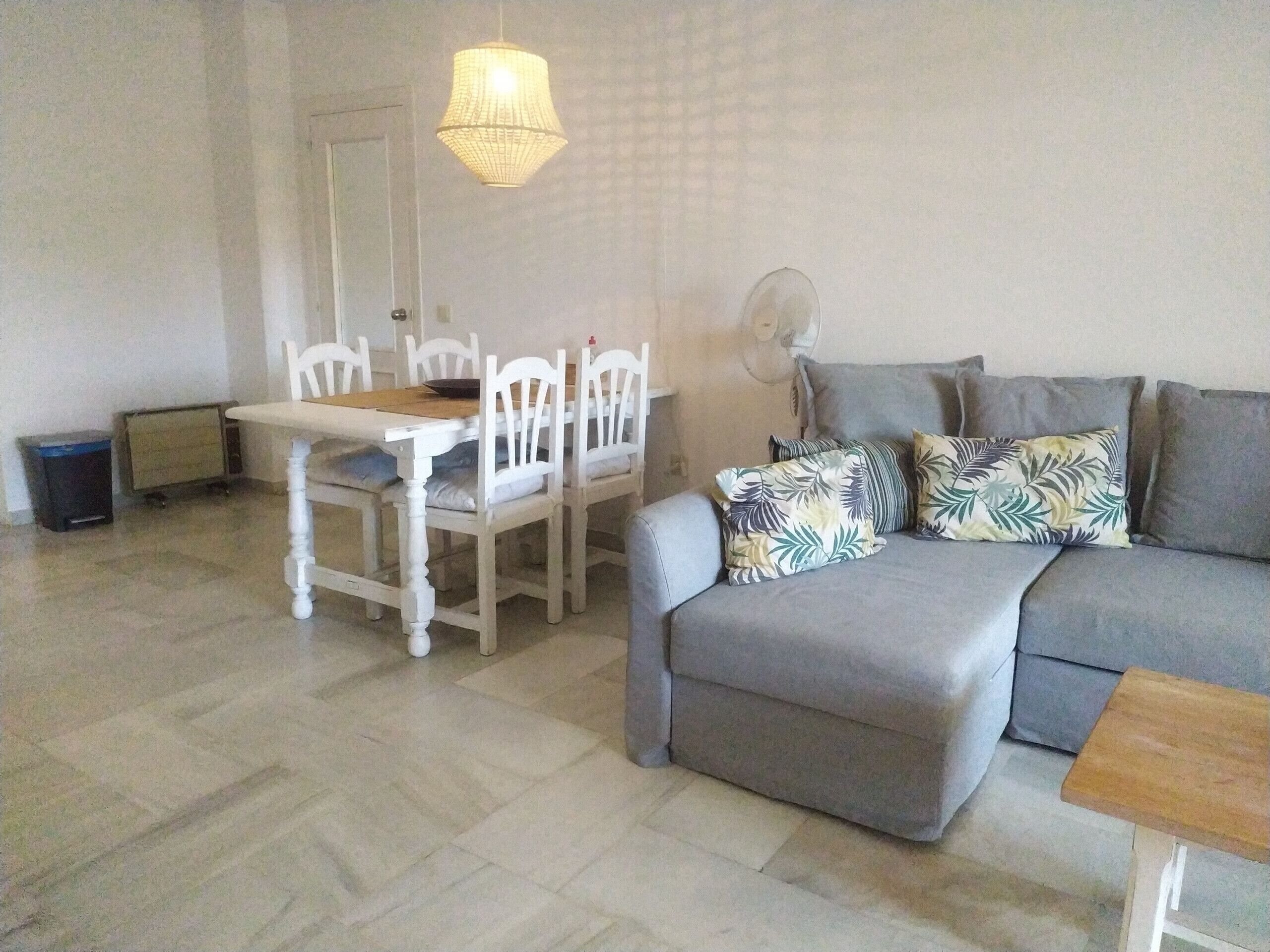 Una sala de estar con un sofá gris, sillas blancas, una mesa de comedor y una lámpara colgante.