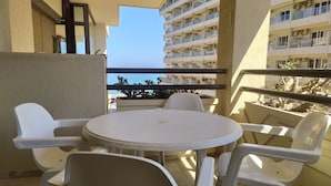 Ein Balkon mit einem runden Tisch und vier Stühlen, mit Blick auf ein Gebäude mit mehreren Balkonen und freiem Meerblick.
