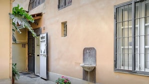 A narrow alleyway with a door, a window with bars, a small sink, and a potted plant. - Rome Studio Historic Center (Roma)