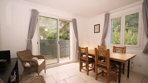 A dining area with a table and chairs, a television, and a sliding glass door leading to a garden.
