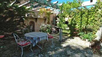 Une terrasse dallée de pierres, avec une table et des chaises, entourée de verdure et agrémentée d’une pergola.
