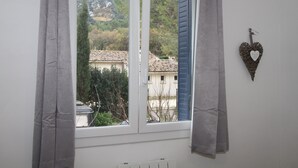 A room with a window overlooking a village, a radiator below, and a heart-shaped decoration on the wall.