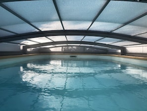 Una piscina interior con techo de vidrio, agua cristalina y un trampolín central.