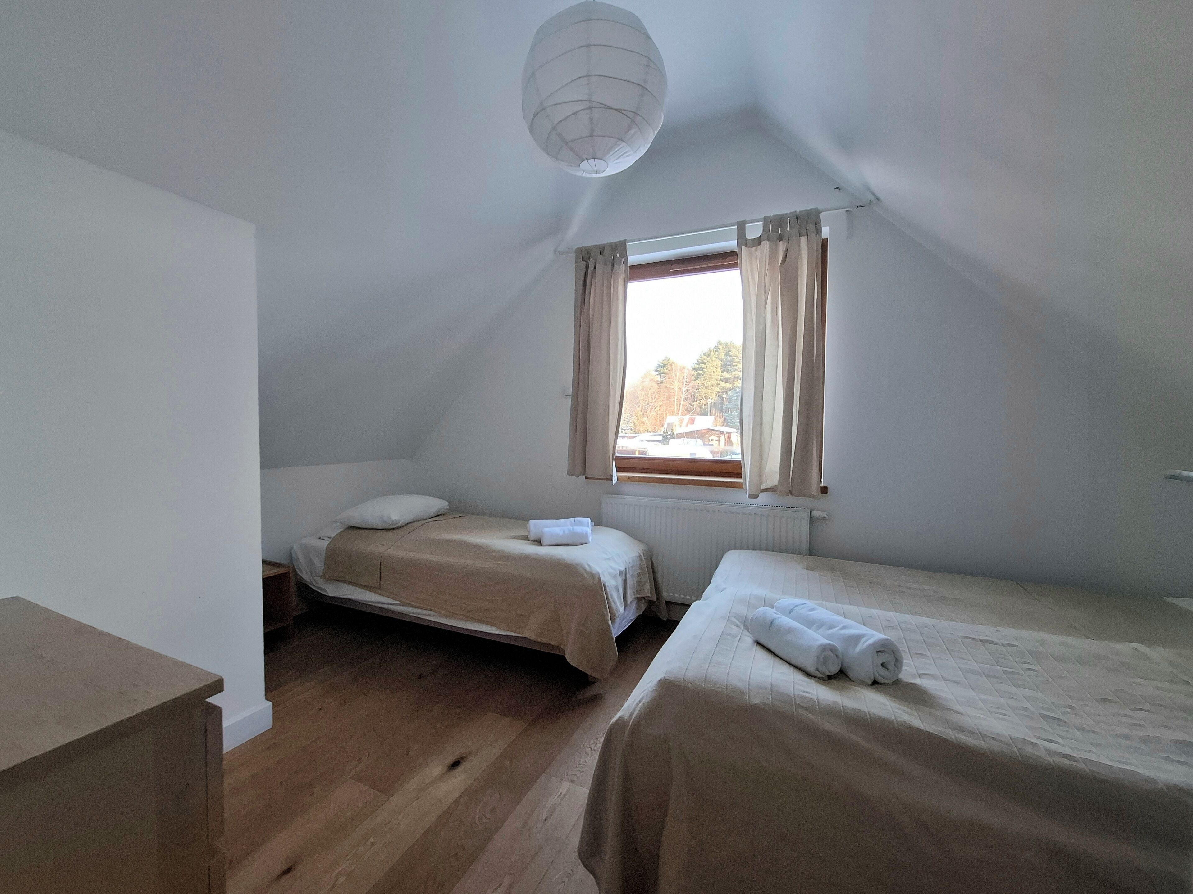 A small, simple room with two beds, a radiator, and a window with curtains.