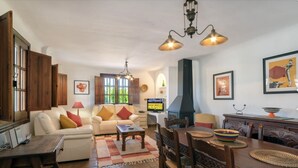 A cozy living room with a sofa, coffee table, and dining table set. There is a fireplace, a television, and artwork on the walls. - Stunning private rural Villa in the Lecrin Valley, Granada with 7mx4m pool (Melegís)