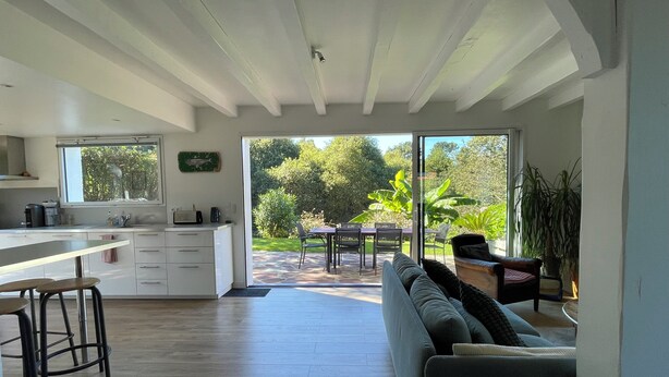Una cocina moderna con un ventanal grande, una zona de comedor con mesa y sillas, y una acogedora sala de estar con sofá y cojines.