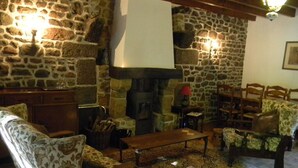 A cozy living room with stone walls, a fireplace, wooden furniture, and a patterned rug.
