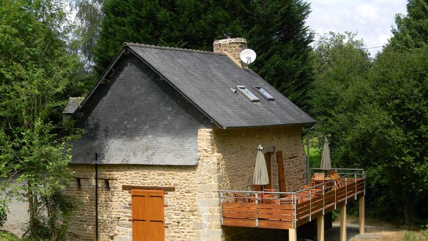 A stone house with a wooden deck, a chimney, and a satellite dish.