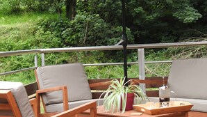 A wooden deck with outdoor furniture, including chairs and a table, and a large umbrella providing shade.