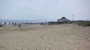 Ein Beachvolleyballfeld mit Netz, einer Schutzhütte und einem Mülleimer.