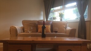 A wooden table with two wine glasses and a bottle of wine in front of a beige sofa with cushions. - Cosy Cornish Bolt Hole, Pet Friendly (Truro)