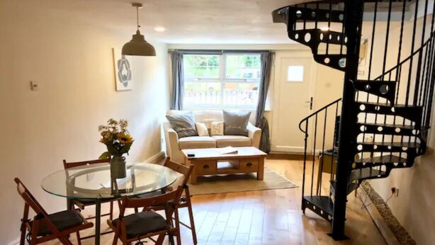 A dining area with a glass table and chairs, a sofa, and a black spiral staircase. - Cosy Cornish Bolt Hole, Pet Friendly (Truro)