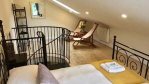 A bedroom with a bed, a chair, a small table with a vase, and a window. - Cosy Cornish Bolt Hole, Pet Friendly (Truro)