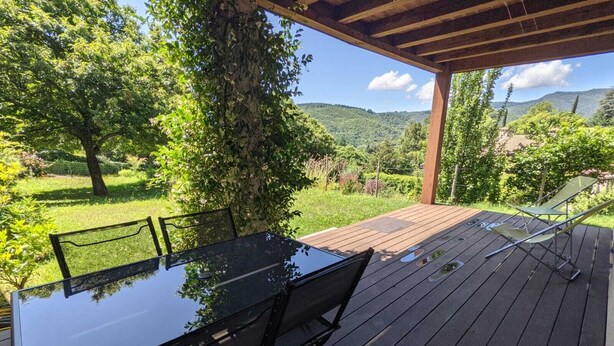 An outdoor deck with a glass-top table and chairs, surrounded by lush greenery and a mountainous backdrop. - Countryside, garden on large plot, with dominant terrace and views (Lasalle)