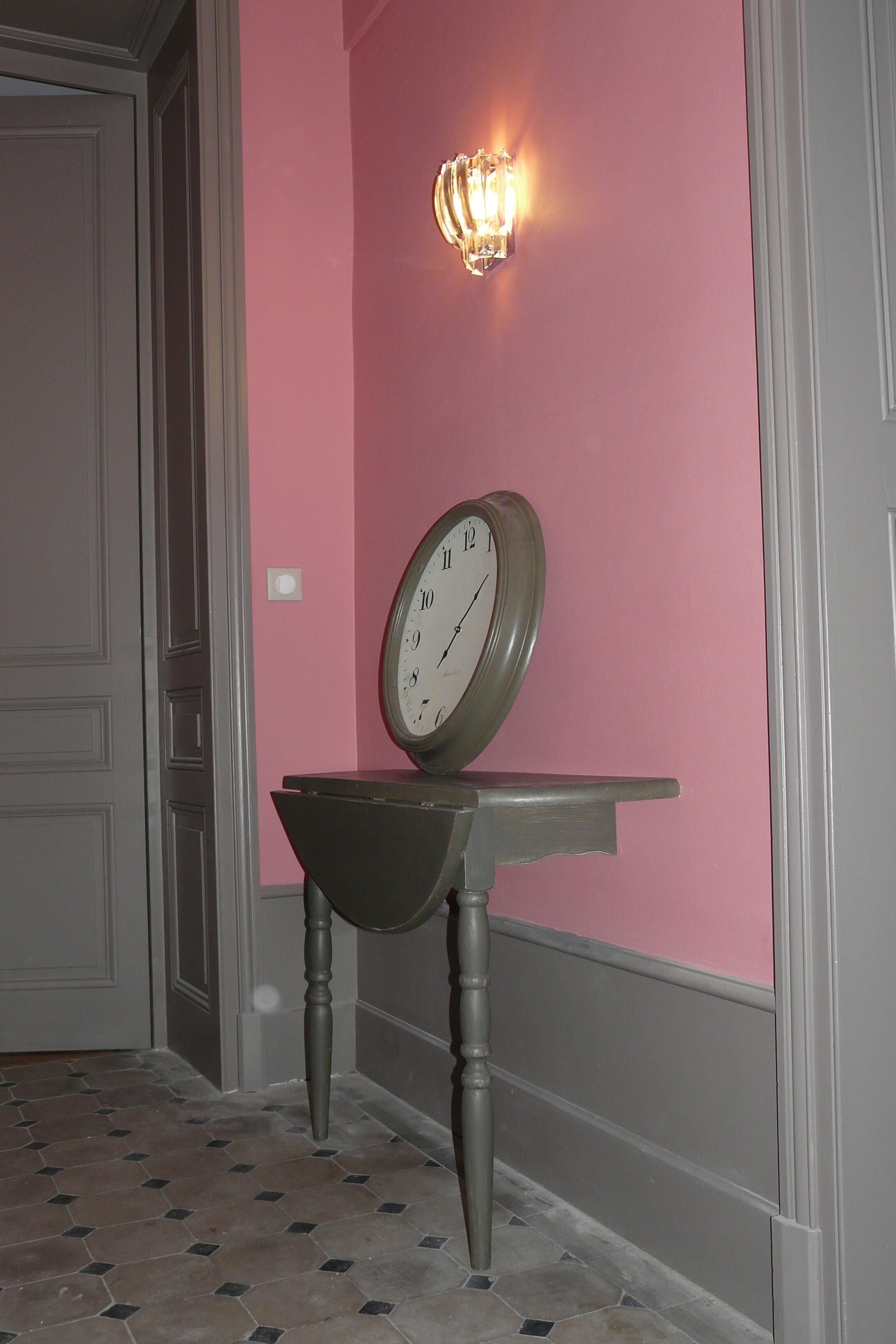 Un pasillo con un reloj de pared, una lámpara y suelo de baldosas.