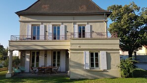 A two-story house with a balcony, a dining area with outdoor furniture, and a small attached structure. - TOWNHOUSE - LYON COUNTRYSIDE - LARGE GARDEN (Grenay)