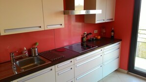 Una cucina moderna con lavello in acciaio inossidabile, mobili bianchi e uno schienale rosso.