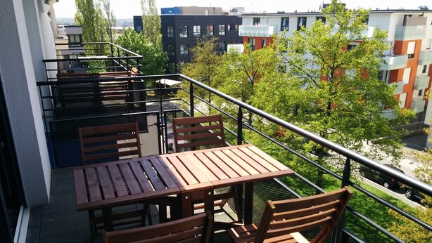 Un balcone con tavoli e sedie di legno, vista su una città con edifici moderni e aree verdi.