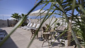 A patio area with lounge chairs and umbrellas, surrounded by potted plants and a concrete wall. - Villa Barletta apartment mansarded in villa on the first floor number 5 (Marina di Acate)
