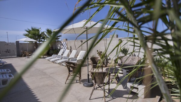 A patio area with lounge chairs and umbrellas, surrounded by potted plants and a concrete wall.