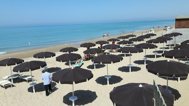 A beach with numerous black umbrellas and sun loungers, a wooden structure in the background, and a clear view of the ocean. - Villa Barletta apartment mansarded in villa on the first floor number 5 (Marina di Acate)