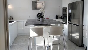 Una cocina moderna con un refrigerador de acero inoxidable, un horno empotrado y un microondas. Hay una mesa de comedor con dos sillas blancas y un florero con flores.