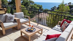 Un balcón con vista al mar, amueblado con un sofá, sillas y una mesa con aperitivos.