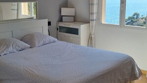 Un dormitorio con cama, mesita de noche, lámpara y ventana con vista al mar.
