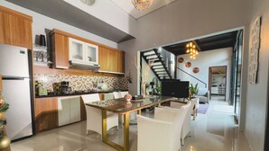 Une cuisine moderne avec un coin repas, comprenant une table en verre, des chaises en osier et un escalier menant à un niveau supérieur.